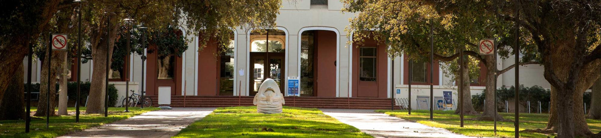 An upside down egghead statue in front of a building on campus. 